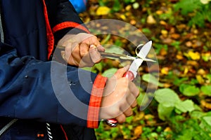 A boy with a knife cleans a stick in the forest. One child plays with a penknife