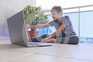 Boy with laptop computer doing sport exercises, practicing yoga on balcony. Sport, healhty lifestyle, active leisure