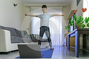 Boy with laptop computer doing sport exercises, practicing yoga at home. Sport, healhty lifestyle, active leisure for