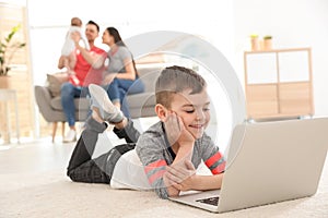 Boy with laptop lying on carpet near his family