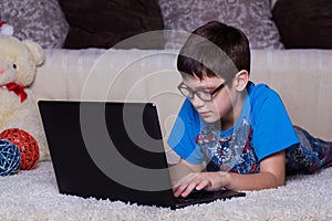 A boy with a laptop lying on the floor at home, on the carpet. Technology, Internet, modern communication concept