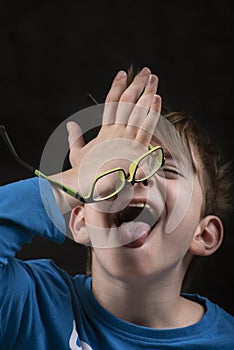 Boy laughs and doing song facepalm. Portrait of fun schoolboy on black background