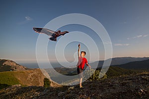 The boy launches a kite. Beautiful sunset. Mountains, sea, landscape. The boy in the red t-shirt and shorts. Summer day