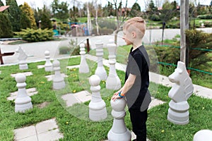 Boy on the lawn with a huge chessboard stands next to a piece and thinks about the next move