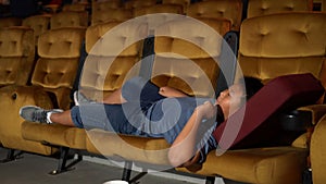 A boy laying down on armchair in cinema.