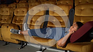 A boy laying down on armchair in cinema.