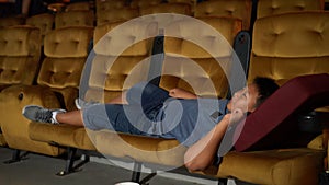 A boy laying down on armchair in cinema.