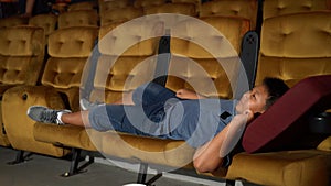 A boy laying down on armchair in cinema.