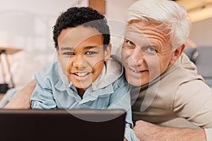 Boy laying at the floor and using tablet while relaxing with his grandfather