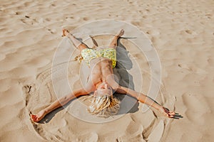 Boy laying on sand beach and playing the angel. Summer time concept. Copy space.