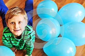 Boy laying on the wooden floor with blue balloons