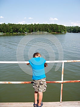 Boy leaning on railing by lake