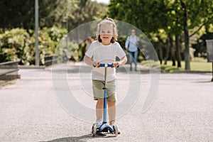 Boy learn to ride scooter in a park on sunny summer day. Preschooler boy riding a roller. Kids play outdoors with scooters