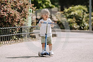 Boy learn to ride scooter in a park on sunny summer day. Preschooler boy riding a roller. Kids play outdoors with scooters