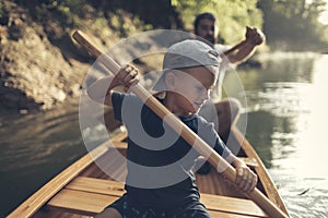 Boy learning to paddle canoe with his dad