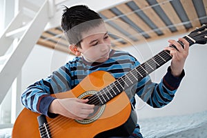 Boy learning to play acoustic guitar. Boy is practicing acoustic guitar in his room