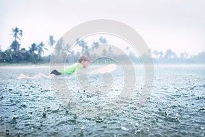 Boy learning to surf under the tropical rain