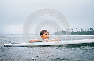 Boy learning to surf under the tropical rain