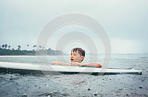 Boy learning to surf under the tropical rain. Surf school education concept image