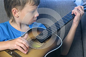 Boy learns to play guitar sitting on the couch. Concept of learning to play a musical instrument.