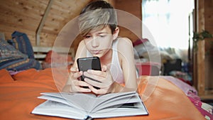 boy lies on the bed pretends to read a book but uses the phone