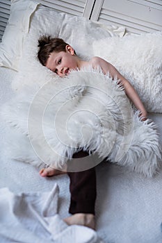 Boy lies on  bed with white bedding,  handsome young man with  pretty face is resting in bed, cozy sleeping place