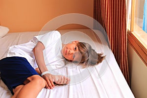 A boy lies on a bed with white sheets in a hotel room.