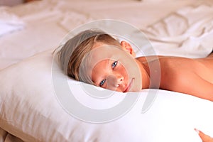 A boy lies on a bed with white sheets in a hotel room.