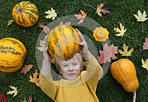 boy lies on the grass among the leaves, large and small pumpkins, one of them holds in front of him