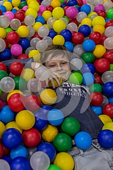 A boy lies among multi-colored plastic balls in a playroom. Happy Birthday party.