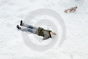 Boy lies in snow, enjoys winter, next to him is dog, happiness, childhood. View from above