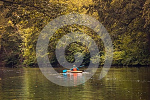 Boy in life jacket doing nature sports canoeing, with a orange canoe on wild river in a autumn color theme.  forest scene use as