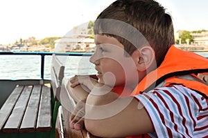 Boy in a life jacket sits on a boat