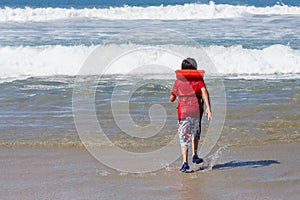 A boy in a life vest runs towards the ocean.