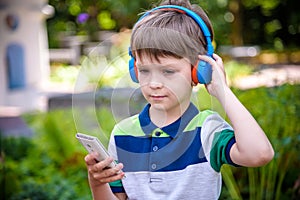 Boy listening music in headphones sitting on the bench and stares at the phone. Warm sunny evening. music relax concept