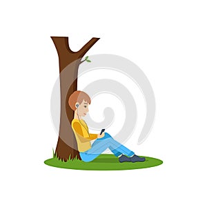 Boy listening to music, near tree in the park.