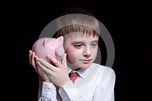 Boy listens attentively to the pink piggy bank. Business concept. Black background