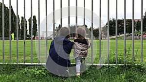 Boy and little girl look at football game from behind fence