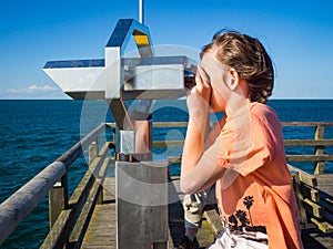 Boy is looking through a binocular at the sea