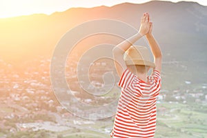 Boy looking at the city from a height. Hands over head. Rear view, sunset time