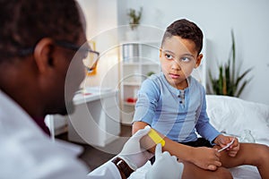 Boy looking at doctor taking care of his wounds after falling