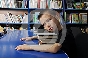 Boy looking groomy tired on pile of book in library don`t want to learning