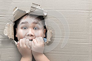 Boy looking through hole on cardboard with shocked face