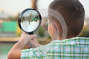 Boy is looking through magnifier in fall park