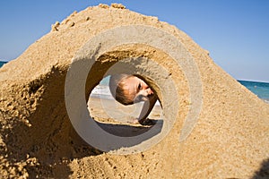 Boy looking through a sand castle on the beach