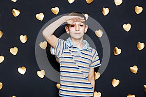 Boy looking for something on golden hearts background