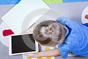 Boy looking at tablet pc, lying on the floor with books