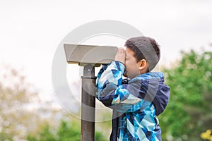Boy looking in telescope in park. Tourists on observation deck