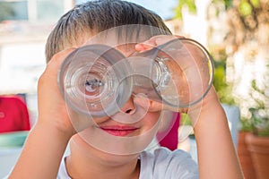 Boy looking through two glasses. Smiling boy. Funny kid joking. Summer vacation. Waiting for order at cafe, cafeteria