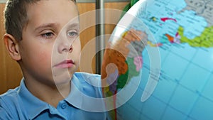 The boy looks attentively at the globe, rotates it, studies the countries.